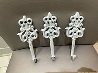 Front view of three identical ornate white metal hooks