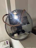 Front view showing round mirror, silver frame, rope handle