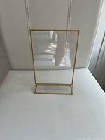 Front view of gold-tone floating photo frame standing on base