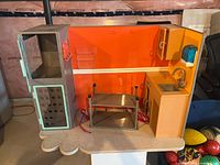 Front view of plastic pet spa playset showing kennel door, sink, soap dispenser, shelf, grooming table and hoses