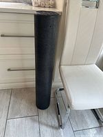 Foam roller standing upright beside chair