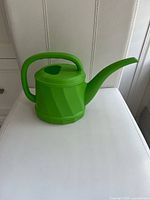 Full view of green plastic watering can on white surface