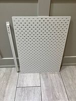 Front view of white SKÅDIS pegboard and separate mounting rail leaning against wall