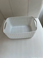 Rectangular white plastic basket with perforated sides and handles displayed on light surface