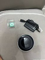 Samsung wireless charger, green Apple iPod Shuffle in case, black USB WiFi adapter with cable displayed on cushion