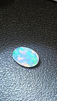 Oval faceted opal on black surface showing multicolored play-of-color