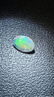 Oval faceted opal with green, blue and orange play-of-color on black background