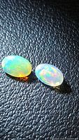 Two oval faceted opals showing color play on textured black background