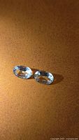 Pair of pale blue oval-cut aquamarines on brown background
