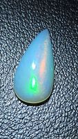 Pear cabochon opal showing play-of-color on textured background