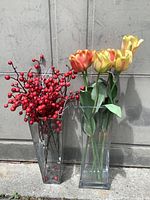 Two tall clear glass square vases with faux tulips and berry stems