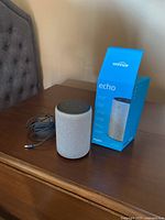 Grey Amazon Echo smart speaker, power adapter, and original box on wooden surface
