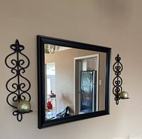 Mirror mounted on wall flanked by two matching metal sconces each with gold candle