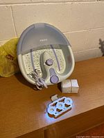 Overall view of HoMedics foot spa bath with cord, roller attachment and small boxed accessory on wooden surface