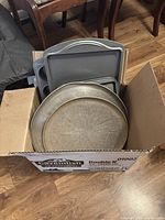 Box containing assorted non-stick bakeware including pizza pans and baking sheets