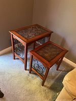 Two wood nesting tables with metal scroll sides and inlaid tops