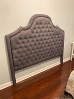Front view of grey upholstered queen headboard showing arched top and tufting