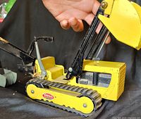 Left side view of yellow Tonka trencher showing tracks, boom, bucket and logo decal