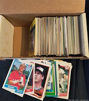 Open cardboard box filled with a stack of trading cards; several cards laid out in foreground showing typical 1990s baseball card designs