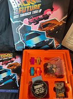 Game box lid, inner plastic insert with coloured DeLorean player pieces, dice bag, tokens, and cards visible