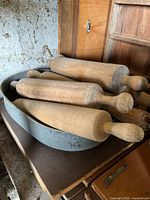 Five wooden rolling pins stacked inside an oval blue speckled enamel roasting pan on a shelf