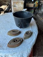Overall lot showing three sad iron bases and black cast iron pot on table