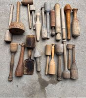 Group of 22 wooden mashers and pestles laid on concrete, showing varied shapes, sizes and patina.