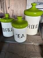 Front view of three white canisters with green lids labeled Coffee, Tea, Flour (two included in lot)