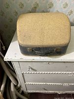 Closed tan/black hard carrying case on dresser