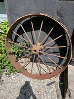 Full view of rusted iron wheel leaning against wall