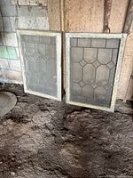 Both leaded glass window panels leaning against wall