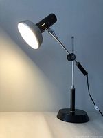 Full view of lit articulating desk lamp showing shade, arm, base