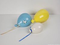 Top view of three ceramic balloons in blue, yellow, white with ribbons