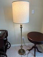 Brass-tone floor lamp with drum shade shown plugged in and lit