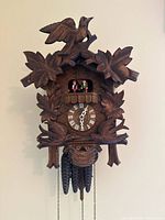 Front view of carved wood cuckoo clock showing bird, leaf carvings, dial and weights