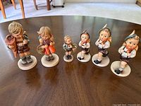 Six Hummel child figurines lined up on table