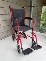 Front-left view showing entire red aluminum transport chair with footrests attached