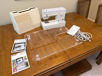 Entire lot on table: sewing machine, hard case, quilting table, manuals, pedal