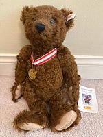Full view of brown Steiff teddy bear with ribbon, medal, ear tag and certificate