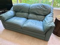 Front view of teal leather loveseat showing cushions and overall condition