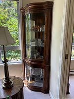 Full view of curio cabinet showing wood frame, curved glass doors, placed in corner