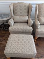 Wingback chair with lumbar pillow beside ottoman showing fabric pattern and leg style