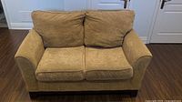 Front view of tan fabric two-seat couch with cushions and wood feet