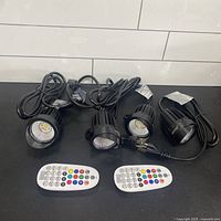 Four spotlights with cords and two remotes displayed on table
