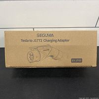 Cardboard box front showing Seguma Tesla to J1772 Charging Adapter labeling