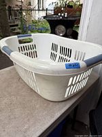 Angled view of white plastic laundry basket showing blue handles and vented sides