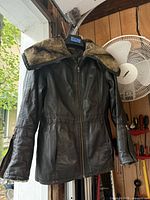 Front view of dark brown Danier leather jacket with faux-fur collar displayed on hanger