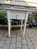 Full view of white-painted wooden table showing drawer and turned legs