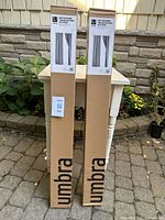 Front view of two boxed Umbra Anywhere tension rod systems