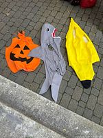 Pumpkin, shark and banana costumes laid out on ground